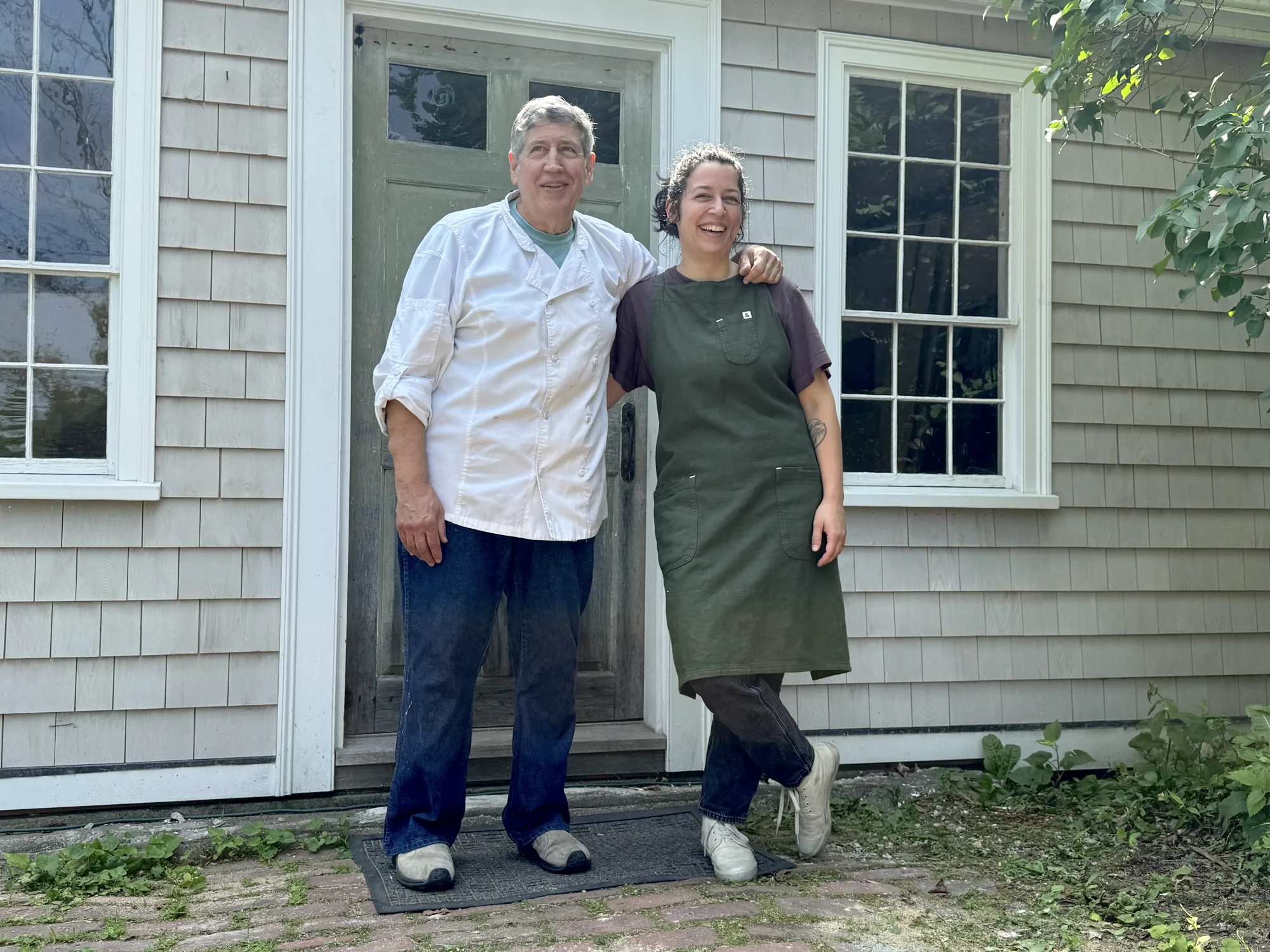 Steve Brill and Emily Clark standing arm in arm outside the shingled 27 Summer Street bakehouse